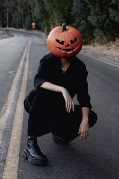 a woman kneeling down on the side of a road with a pumpkin hat on her head