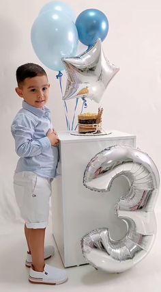 a young boy standing in front of a cake and balloons with the number three on it