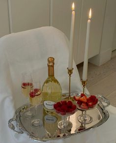 there is a tray with wine and strawberries on the table next to two candles