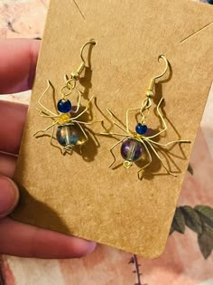 a pair of gold spider earrings with blue glass beads on it's earwires