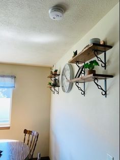 a dining room table with chairs and two shelves on the wall above it that have clocks