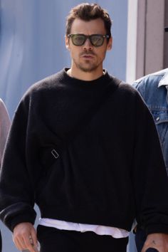 a man in black sweater and sunglasses walking down the street with his hand on his hip