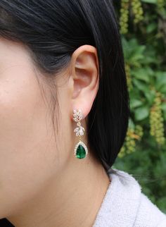 a close up of a person wearing some kind of earring with green and white stones