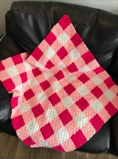 a pink and white checkered blanket sitting on top of a black leather chair next to a