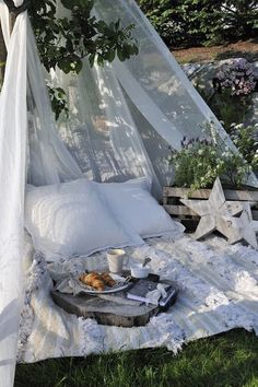 a bed covered in white sheets and pillows under a tree with stars on the ground