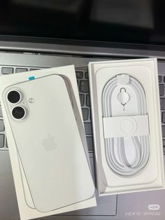 an apple phone in its box next to it's charger and cable plugged into the computer