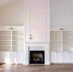 an empty living room with white bookcases and a fireplace