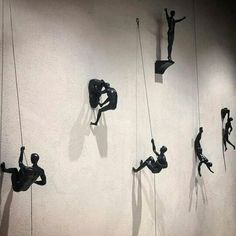 several sculptures are hanging on the wall with ropes and people climbing up to their feet