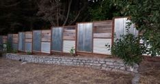 a row of metal and wood fences next to a stone wall with trees in the background