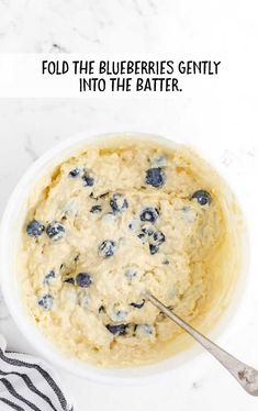 a bowl filled with batter and blueberries on top of a table next to a striped towel