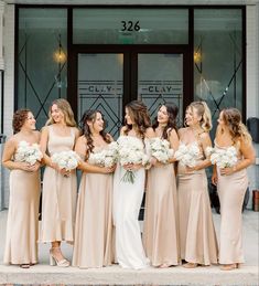 a group of women standing next to each other in front of a building holding bouquets