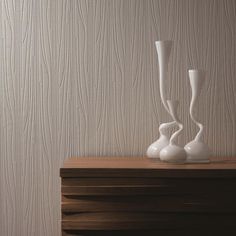 two white vases sitting on top of a wooden table next to a wallpaper