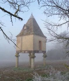 an old building sitting in the middle of a foggy field with trees around it