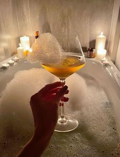 a person holding a wine glass in a bathtub filled with soap and water next to candles