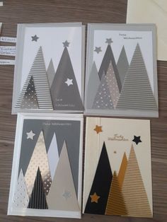 four christmas cards with trees and stars on them, sitting on a table next to envelopes