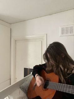 a woman with long hair playing an acoustic guitar in front of a white cabinet and door