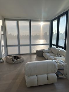 a living room filled with white furniture and large windows overlooking the cityscape in the distance