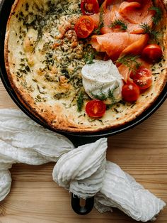 an omelet with tomatoes, cheese and herbs on it sitting on a wooden table