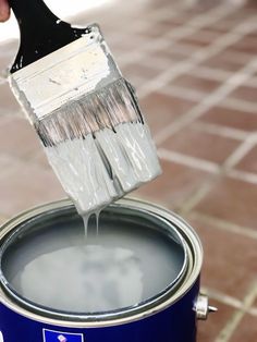 a person is holding a paint brush over a blue bucket with white paint on it