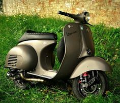 a scooter parked in the grass near a brick wall