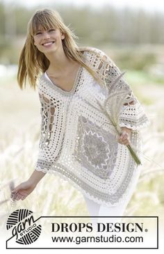 a woman standing in a field holding a flower and wearing a crocheted sweater