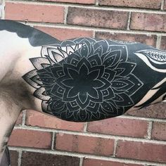 a man with a black and white flower tattoo on his arm, standing in front of a brick wall