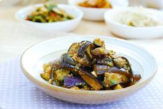 a white bowl filled with cooked eggplant and other food on top of a table