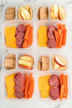 four plastic containers filled with meat, cheese and fruit on top of a marble counter