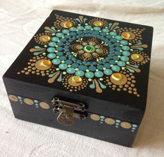 an ornate wooden box with gold, blue and green designs on the lid sitting on a white sheet