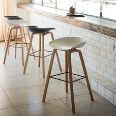 three bar stools sitting in front of a white brick wall and counter with windows