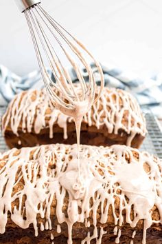 two loaves of bread covered in icing on top of a cooling rack with a whisk