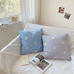 a white bed with blue pillows and pictures on the wall next to it, along with an open book