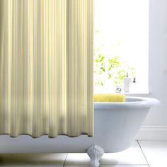 a bath tub sitting next to a window covered in yellow shower curtaines and white fixtures