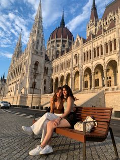 two women sitting on a bench in front of a large building with towers and domes