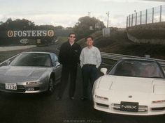 two men standing next to some cars in front of a sign that says fosterso