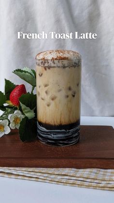 a glass filled with liquid sitting on top of a wooden table next to a flower