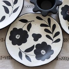 three black and white plates sitting on top of a tablecloth with flowers painted on them