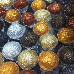 there are many different colored cupcakes in the box together, all with gold and silver glitter on them