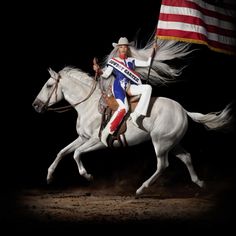 a man riding on the back of a white horse with an american flag in the background