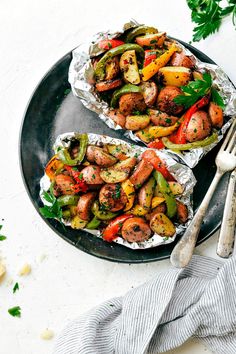 two foil packets filled with vegetables on top of a black plate