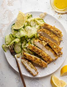 a white plate topped with sliced up chicken and cucumbers next to a fork