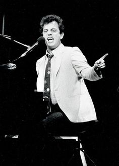 a black and white photo of a man in a suit singing into a microphone while sitting at a piano