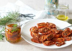 a white plate topped with sliced tomatoes next to a jar of pickles and herbs