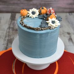 a blue frosted cake with flowers on top sitting on a white plate next to a red place mat