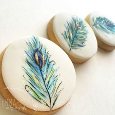 three decorated cookies with blue feathers on them