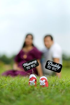 two people are sitting in the grass and one is holding a sign that says mommy to be