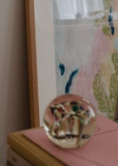 a glass object sitting on top of a pink table next to a framed painting and wooden frame