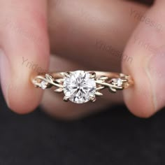 a woman's hand holding an engagement ring with a diamond in the center and leaves on it