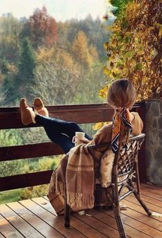 a woman sitting on top of a wooden bench next to a tree covered hillside in fall colors