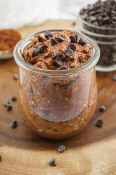 two jars filled with chocolate pudding on top of a wooden table next to other desserts